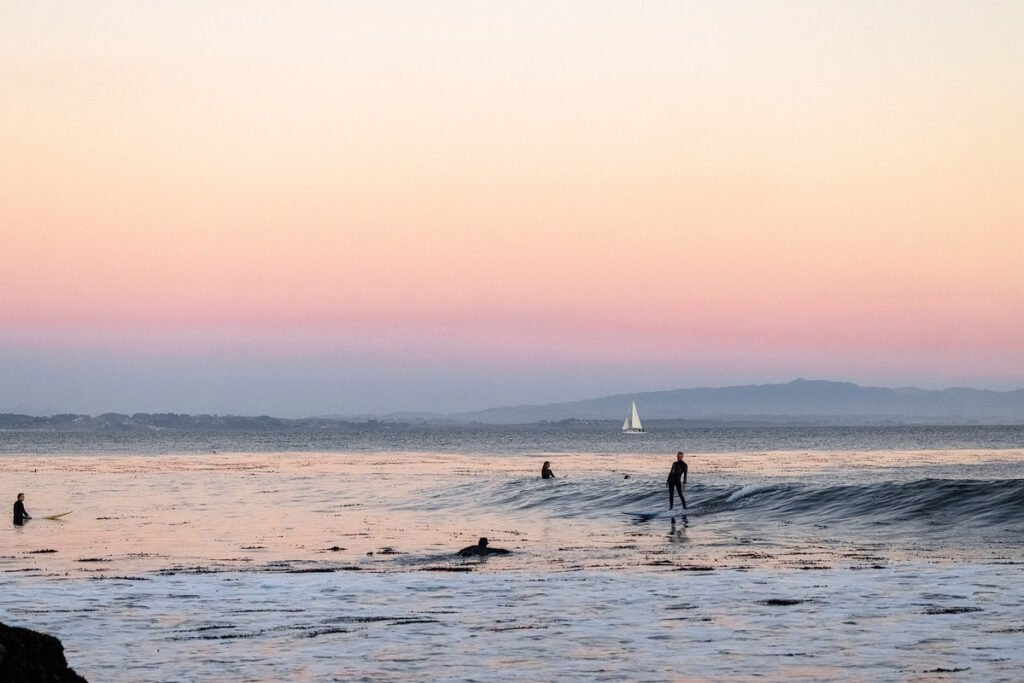 Sunset with surfers in ocean, photo by Ryan Chachi Craig