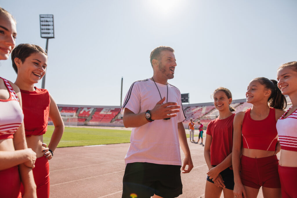 Athletics coach on a sports stadium, leading a team of young athletes.