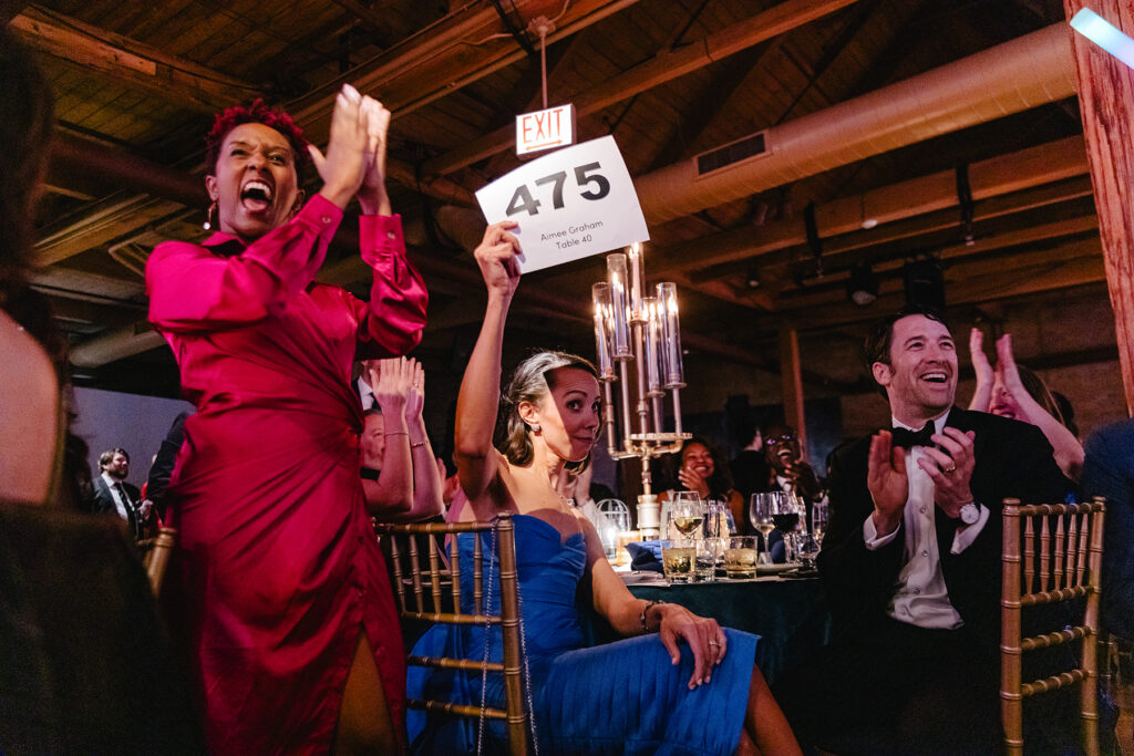 (left to right) Ensemble Member Celeste M. Cooper cheers on Trustee Aimee Graham as she bids on the live auction. Photo by Kyle Flubacker.