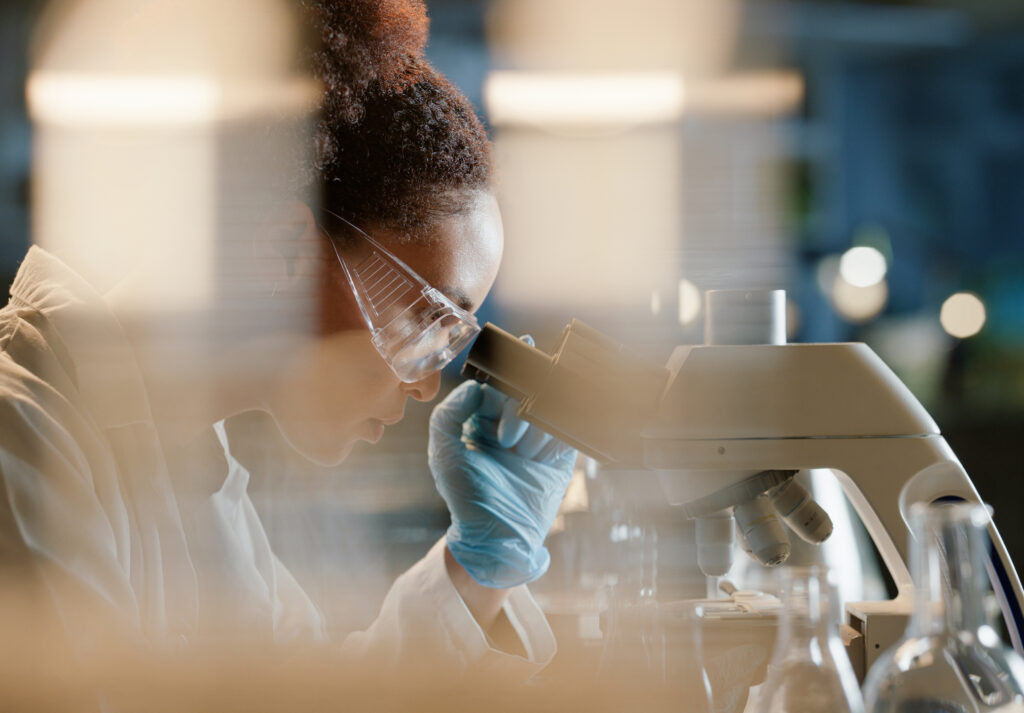 African woman, microscope and medical science in laboratory for research, analytics and medicine. Female scientist, working and experiment or study for results, virus vaccine, and innovation