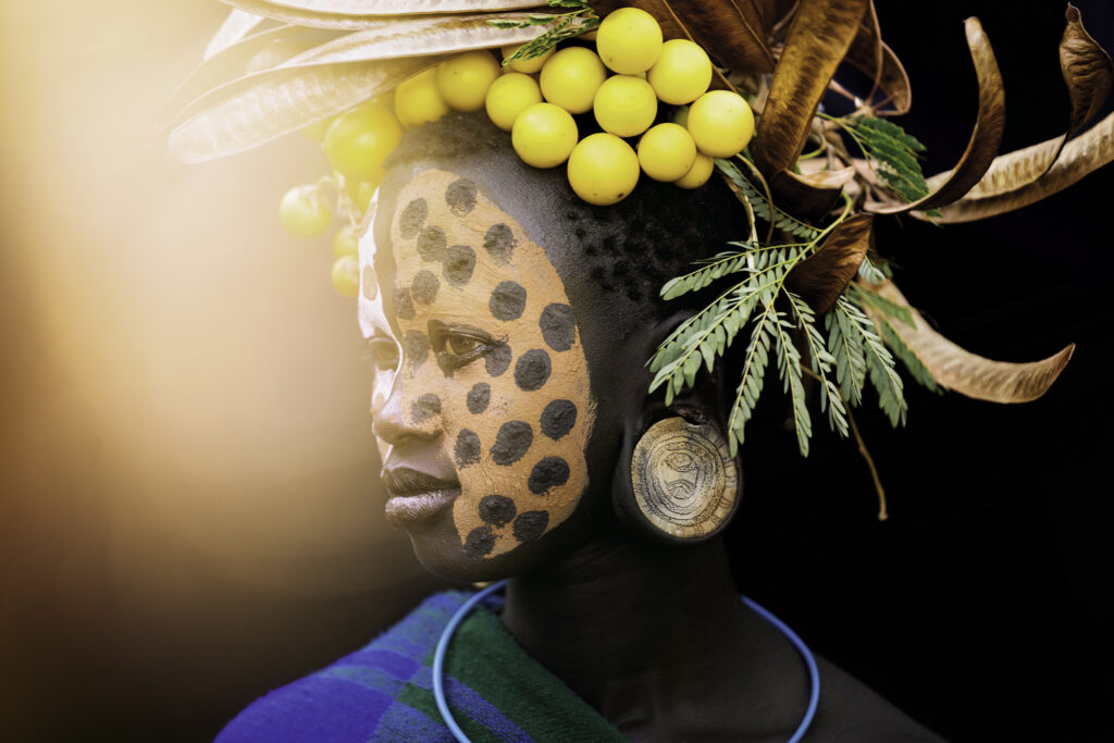 Wearing a crown made of wild tomatoes and seed pods, this Suri girl stares at the rising sun. Omo Valley, Ethiopia.