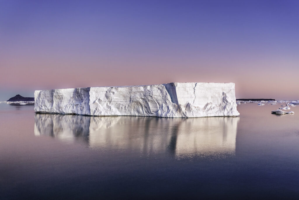 Tabular icebergs glide silently overcalm waters.