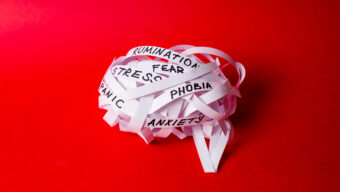 Strips of paper twisted into ball in shape of brain with words STRESS, ANXIETY, PANIC on red background. Tangled thoughts concept, complex mental state