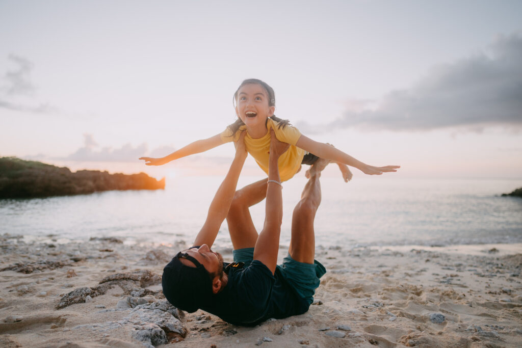 Dad and his young daughter playing airplane on beach at sunset, Japan