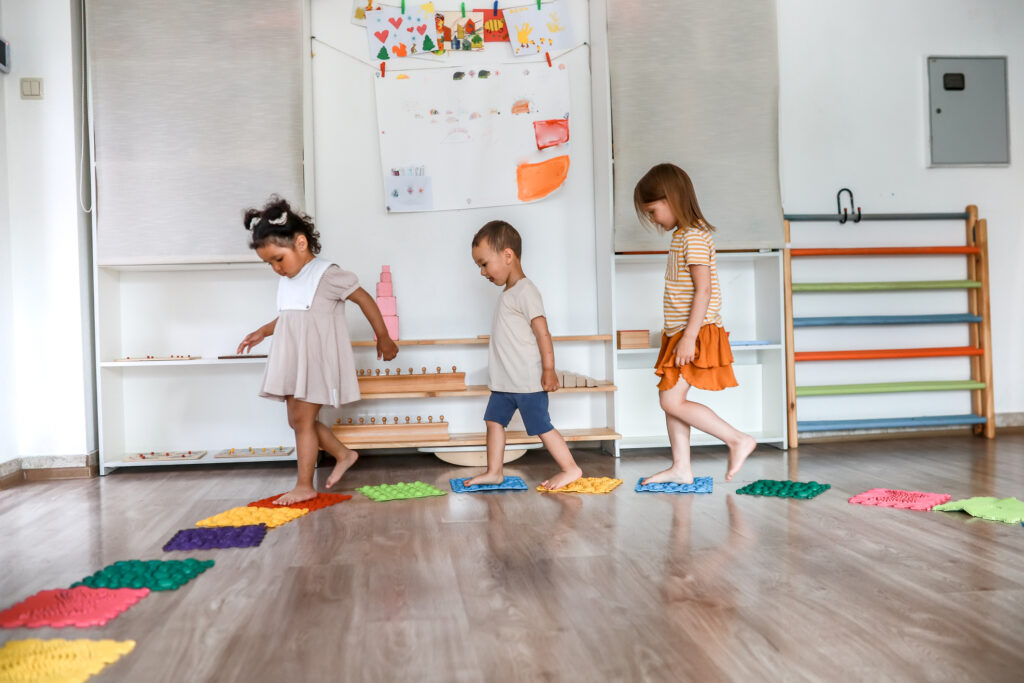 Prevention of flat feet in kindergarten. Toddler children walk on massage children's mats while playing sports indoors in kindergarten.Children's educational activity. Cognitive activity of preschoolers. Creativity and learning. Kindergarten, primary school. Sunday school.Development of intelligence.