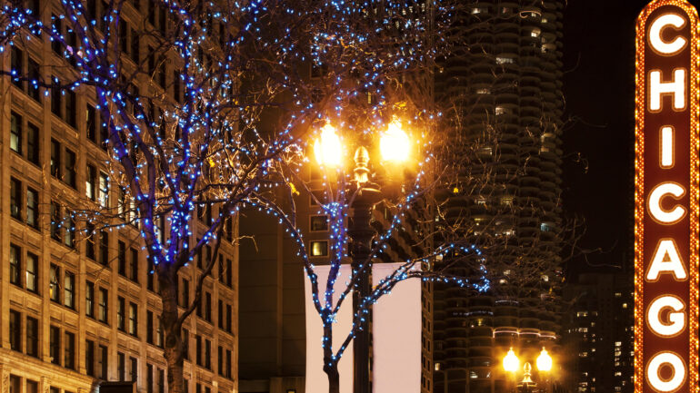 Photo of Chicago's Illuminated sign, at night. Buildings and trees with christmas ornaments.