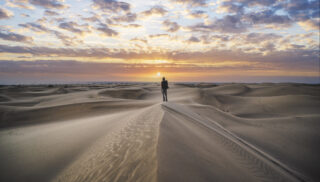 Explorer standing on top of a sand dune at sunrise