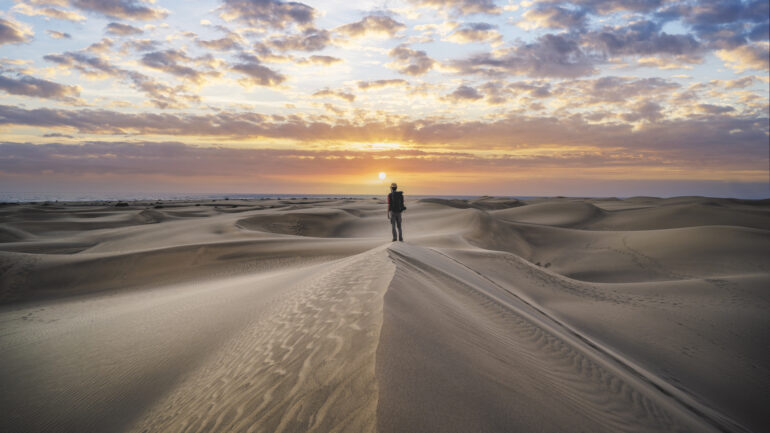 Explorer standing on top of a sand dune at sunrise