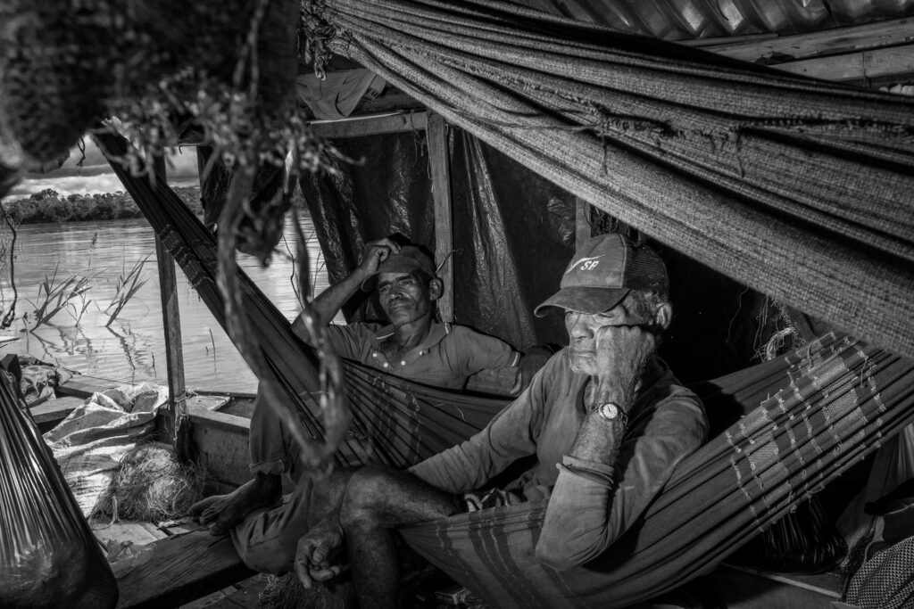 SANTA CRUZ, BRAZIL – JUNE 16, 2022: Antonio (left) with his father on their boat along the Itaquai River, near the riverine community of Santa Cruz, 15 km from Atalaia do Norte. A fisherman by trade, Antonio has twice been fined for catching pirarucu inside Indigenous reserves. In the Vale do Javari, illegal fishing of pirarucu—one of the world’s largest freshwater fish—is not just a subsistence practice but part of a wider criminal economy linked to trafficking and violence, which has placed Indigenous patrols and local communities under constant threat.
