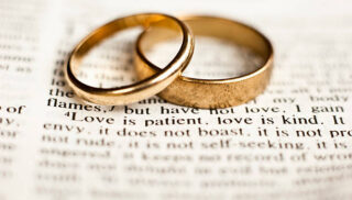 Wedding rings sitting on the 1 Corinthians 13 Bible passage on what love is.