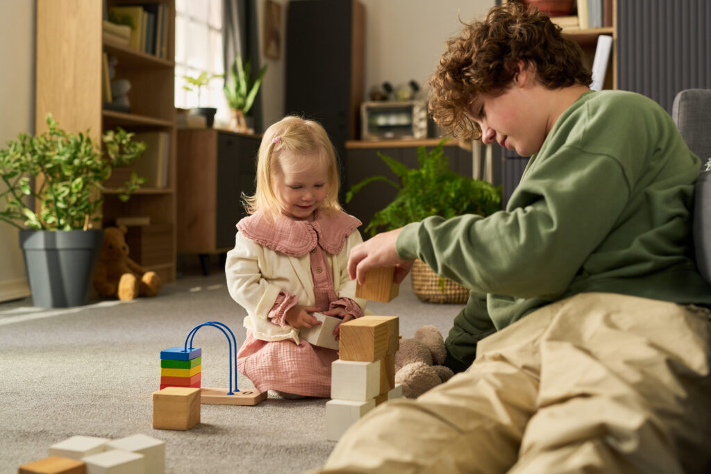 Teenage Boy Helping Young Girl Building Wooden Blocks